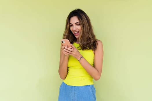 Young woman in casual wear isolated on green background looking at phone screen with big smile reading message