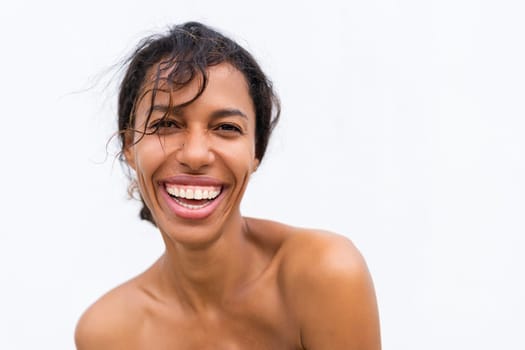 Beauty portrait of young topless african american woman with bare shoulders on white background with perfect skin and natural makeup positive laughing