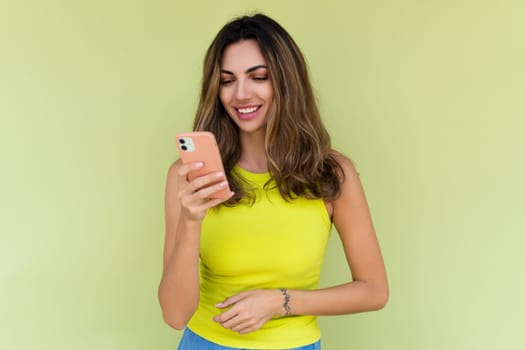 Young woman in casual wear isolated on green background looking at phone screen with big smile reading message