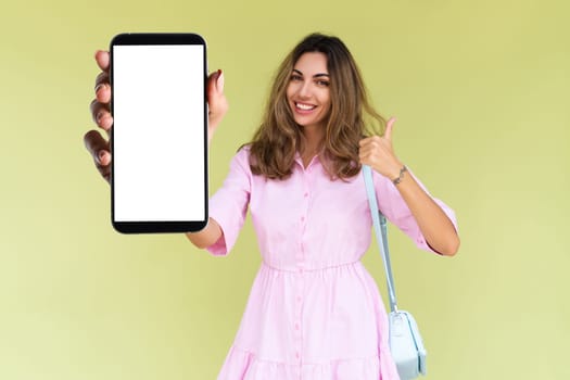 Young woman in casual wear isolated on green background holds a phone with a blank white screen