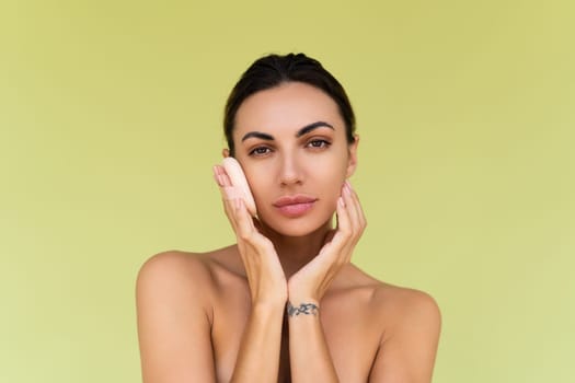 Beauty portrait of young woman with bare shoulders on green background with cosmetic powder puff velour makeup foundation blender sponge applicator