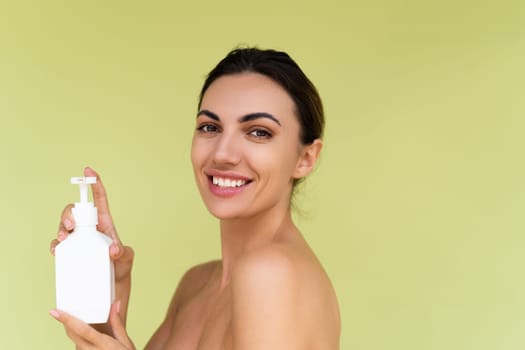 Beauty portrait of young topless woman with bare shoulders on green background with perfect skin and natural makeup holding bottle of shampoo, body lotion