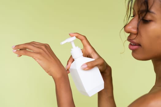 Beauty portrait of young topless african american woman with bare shoulders on green background with white bottle of body lotion
