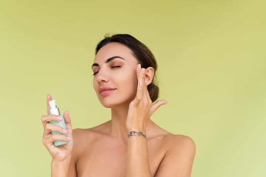 Beauty portrait of young topless woman with bare shoulders on green background with perfect skin and natural makeup holds serum for youth and skin hydration