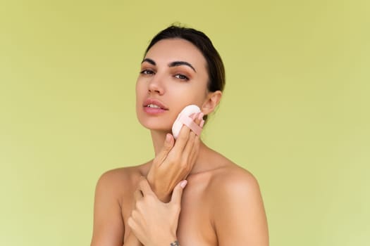 Beauty portrait of young woman with bare shoulders on green background with cosmetic powder puff velour makeup foundation blender sponge applicator