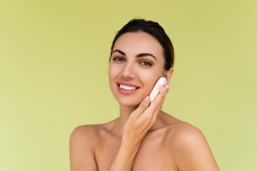 Beauty portrait of young woman with bare shoulders on green background with cosmetic powder puff velour makeup foundation blender sponge applicator