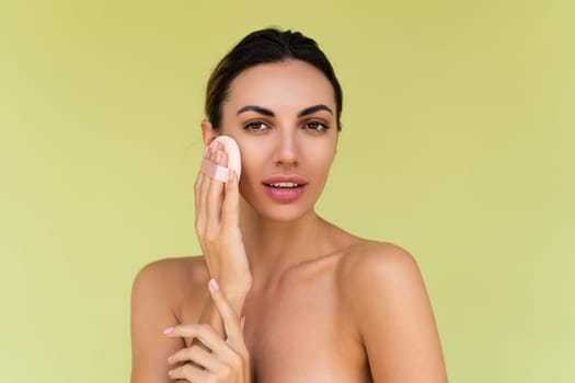 Beauty portrait of young woman with bare shoulders on green background with cosmetic powder puff velour makeup foundation blender sponge applicator