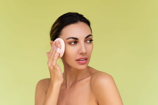Beauty portrait of young woman with bare shoulders on green background with cosmetic powder puff velour makeup foundation blender sponge applicator