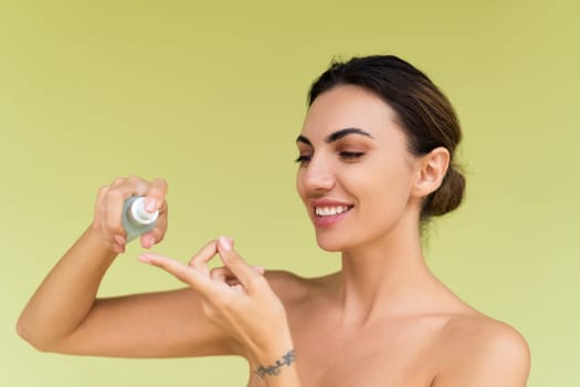 Beauty portrait of young topless woman with bare shoulders on green background with perfect skin and natural makeup holds serum for youth and skin hydration