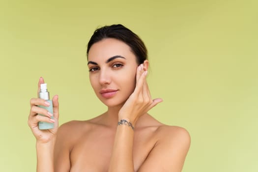 Beauty portrait of young topless woman with bare shoulders on green background with perfect skin and natural makeup holds serum for youth and skin hydration