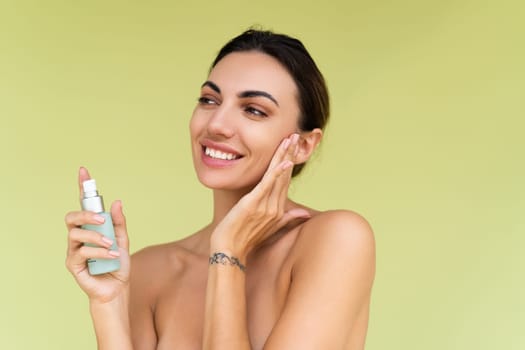 Beauty portrait of young topless woman with bare shoulders on green background with perfect skin and natural makeup holds serum for youth and skin hydration