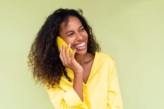 Beautiful african american woman in casual shirt on green background talk on mobile phone smile and laugh