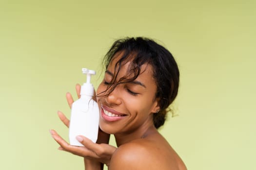 Beauty portrait of young topless african american woman with bare shoulders on green background with white bottle of body lotion