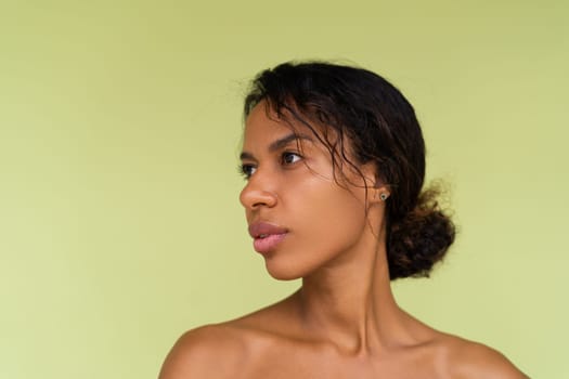 Beauty portrait of young topless african american woman with bare shoulders on green background with perfect skin and natural makeup