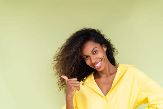 Beautiful african american woman in casual shirt on green background happy positive excited point finger to the left
