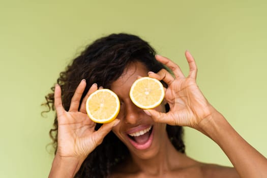 Beauty portrait of young topless woman with bare shoulders on green background with perfect skin and natural makeup holds citrus lemons