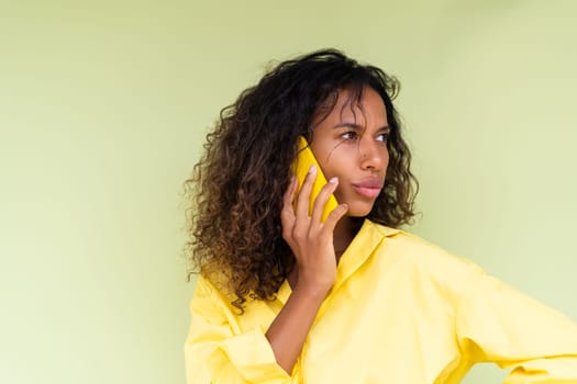 Beautiful african american woman in casual shirt on green background talk on mobile phone shocked confused