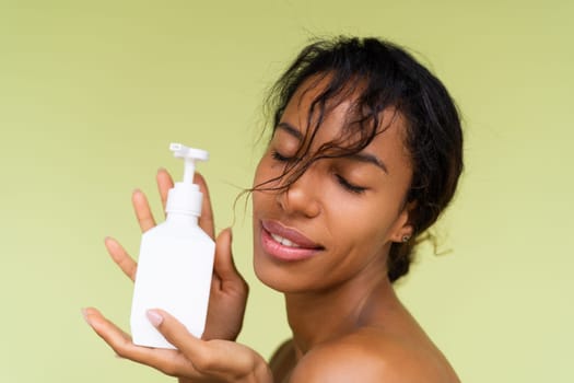 Beauty portrait of young topless african american woman with bare shoulders on green background with white bottle of body lotion