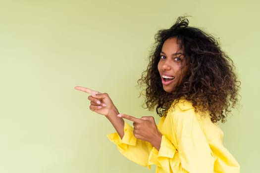 Beautiful african american woman in casual shirt on green background happy positive excited point finger to the left