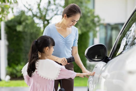 Progressive lifestyle of mother and daughter who have just returned from school in an electric vehicle that is being charged at home. Electric vehicle powered by sustainable clean energy.