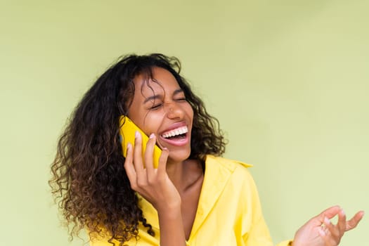 Beautiful african american woman in casual shirt on green background talk on mobile phone smile and laugh