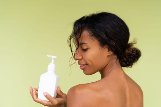 Beauty portrait of young topless african american woman with bare shoulders on green background with white bottle of body lotion