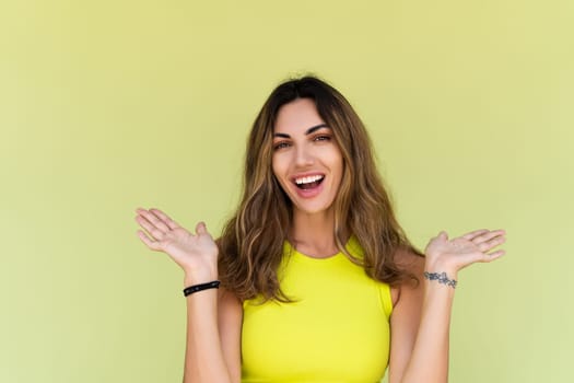 Young brunette in casual wear isolated on green background happy look to camera shocked amazed surprised open mouth