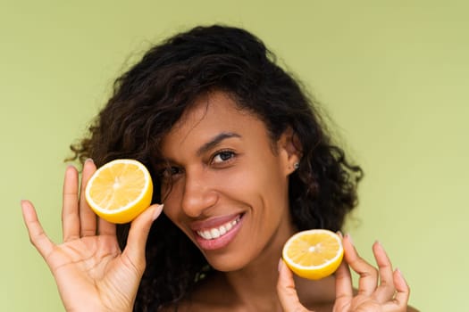 Beauty portrait of young topless woman with bare shoulders on green background with perfect skin and natural makeup holds citrus lemons