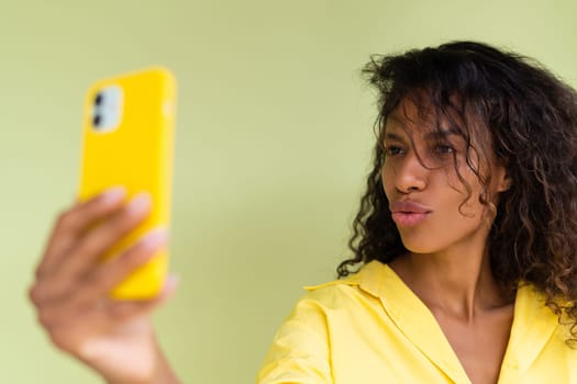 Beautiful african american woman in casual shirt on green background happy taking photo selfie on smart phone
