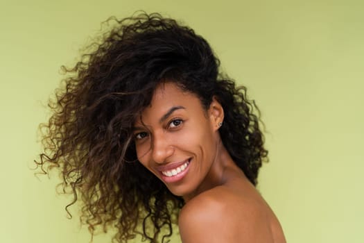 Beauty portrait of young topless african american woman with bare shoulders on green background with perfect skin and natural makeup