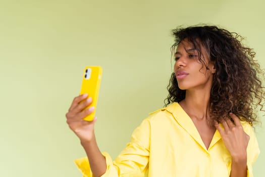 Beautiful african american woman in casual shirt on green background happy taking photo selfie on smart phone