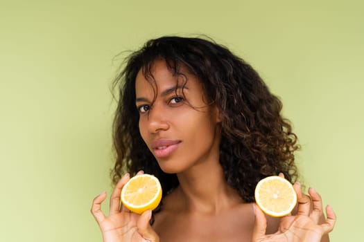 Beauty portrait of young topless woman with bare shoulders on green background with perfect skin and natural makeup holds citrus lemons