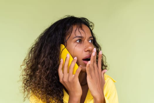 Beautiful african american woman in casual shirt on green background talk on mobile phone shocked confused
