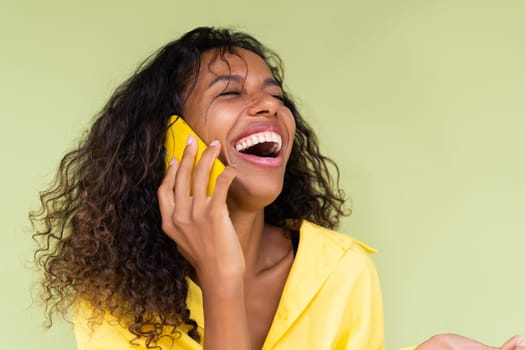 Beautiful african american woman in casual shirt on green background talk on mobile phone smile and laugh