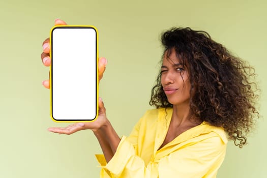 Beautiful african american woman in casual shirt on green background holds a phone with a blank white screen