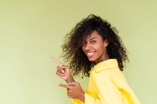 Beautiful african american woman in casual shirt on green background happy positive excited point finger to the left