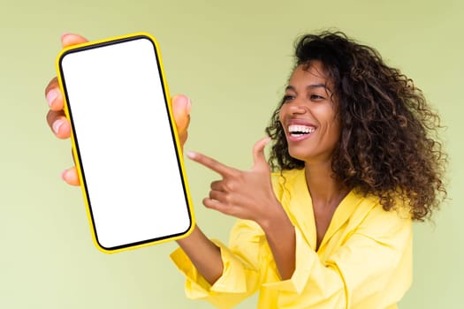 Beautiful african american woman in casual shirt on green background holds a phone with a blank white screen