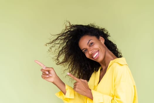 Beautiful african american woman in casual shirt on green background happy positive excited point finger to the left