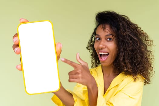 Beautiful african american woman in casual shirt on green background holds a phone with a blank white screen