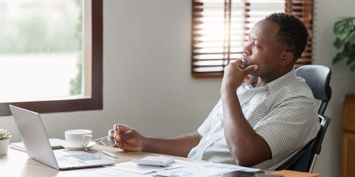 Tired American African business man in stress works with many paperwork document. migraine attack. Freelance, work from home.