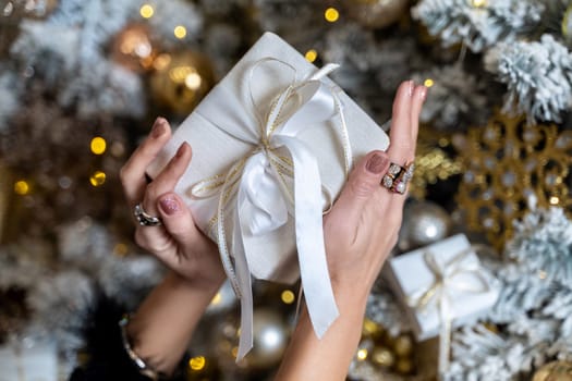 Female hands hold a gift box tied with a ribbon on the background of a Christmas tree, the concept of christmas and gifts
