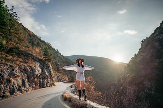 Woman road mountain. A woman in a white sweater, black boots and a hat walks along a winding alpine path between the mountains at sunset in late summer. The concept of travel