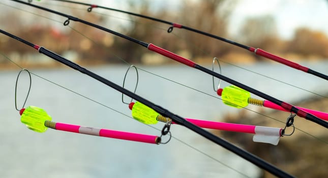 The bite alarm hangs on a fishing rod against the background of water. Fishing rod while fishing on the lake, river. Fishing tackle. Carp rod on a stand with a bite alarm on the line