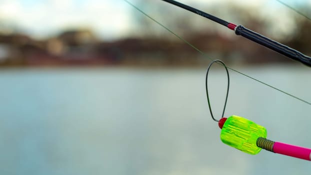 The bite alarm hangs on a fishing rod against the background of water. Fishing rod while fishing on the lake, river. Fishing tackle. Carp rod on a stand with a bite alarm on the line