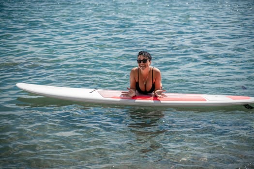 Woman sap sea. Sports girl on a surfboard in the sea on a sunny summer day. In a black bathing suit, he lies on a sap in the sea. Rest on the sea