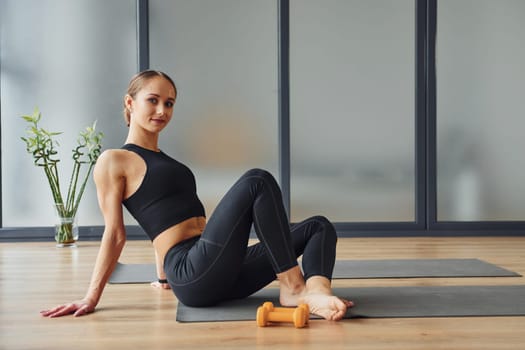 Sits on the mat. Young woman in sportive wear and with slim body have fitness yoga day indoors.