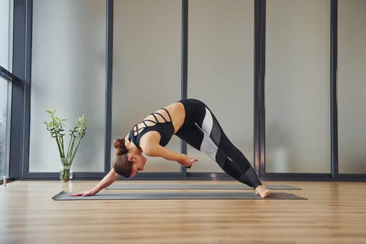 Concentrated on exercise. Young woman in sportive wear and with slim body have fitness yoga day indoors.