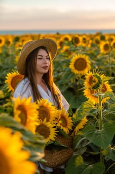 A girl in a hat on a beautiful field of sunflowers against the sky in the evening light of a summer sunset. Sunbeams through the flower field. Natural background