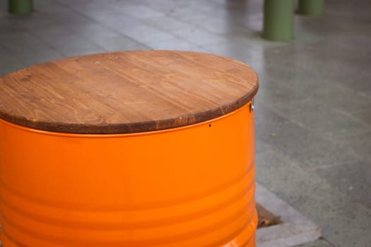 An orange barrel with a wooden table top is a table in an outdoor cafe. The second life of things. Conscious consumption.