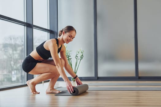 Exercises begins. Young woman in sportive wear and with slim body have fitness yoga day indoors.